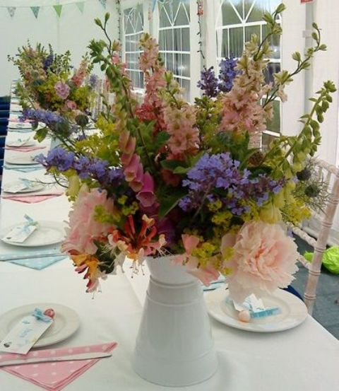 a bold wedding centerpiece of a white metal jug with pastel blooms and greenery is a lovely idea for a summer wedding