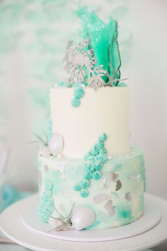 a bright and cool mermaid bridal shower cake in white and greens imitating the sea - seashells, meringues, air plants and waves on top