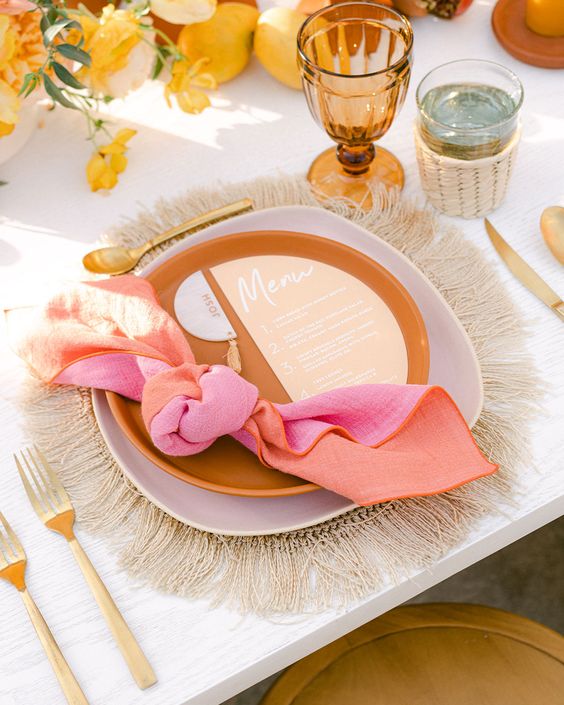 a bright retro bridal shower tablescape with a woven placemat, a lilac and rust plate, a colorful napkin, an amber glass and bodl blooms