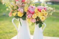 a bright spring or summer wedding centerpiece of two jugs, with pink and yellow blooms and greenery