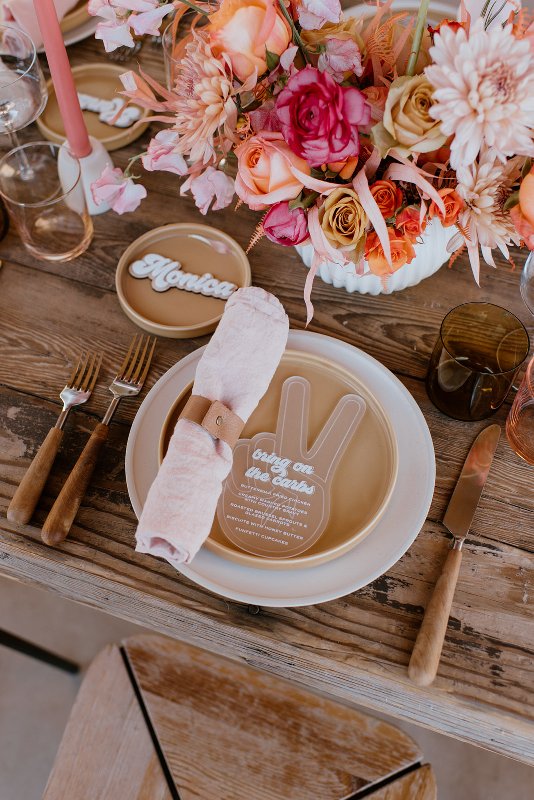 a colorful retro brdail shower table setting with a neutral and tan plate, a blush napkin, colorful blooms and a pink candle