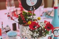 a colorful retro bridal shower centerpiece of a teapot with bold blooms, a vinyl, candles and colorful candles in teacups is pure fun