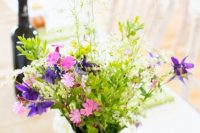 a creamy jug wedding centerpiece of pink, purple and green blooms and lots of greenery is a cool idea for a summer wedding