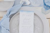 a dreamy ocean-inspired tablescape with blue linens, pebbles, candles, grey lace plates and an ombre menu