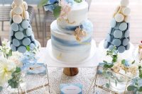 a lovely blue mermad bridal shower dessert table with a watercolor cake with pastel blooms, blush and blue macarons and neutral blooms