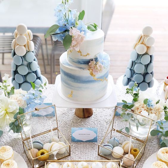 a lovely blue mermad bridal shower dessert table with a watercolor cake with pastel blooms, blush and blue macarons and neutral blooms