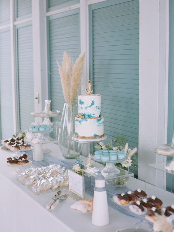 a lovely mermaid bridal shower dessert table with a white cake with turquoise brushstrokes, blue macarons, meringues and eclaires