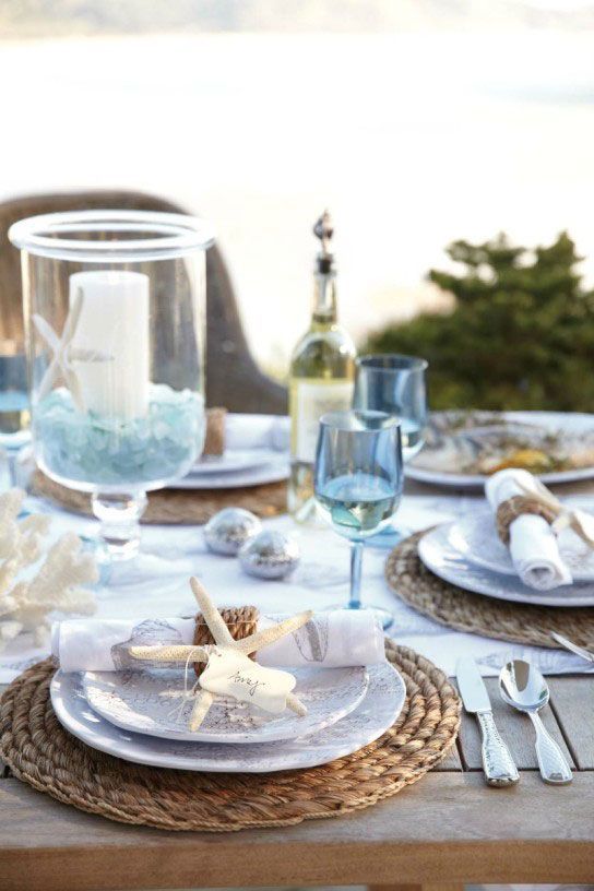 a lovely mermaid bridal shower table setting with woven placemats, printed plates, starfish and blue glasses