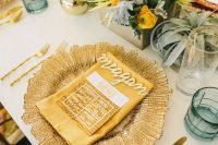 a mid-century modern bridal shower tablescape with a gold placemat, a gold napkin, gold cutlery, bright blooms and greenery and billy balls