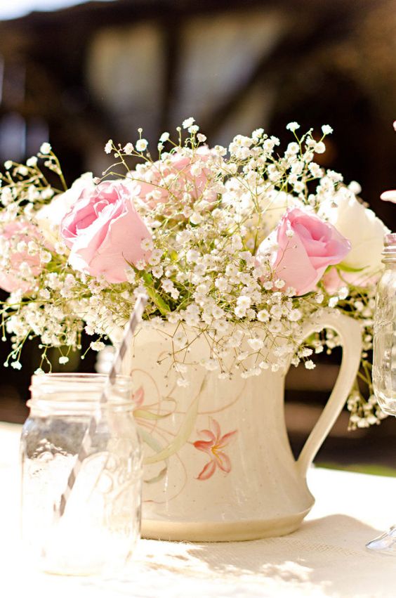 a neutral spring or summer wedding centerpiece of a white floral jug with white and pink roses and baby's breath
