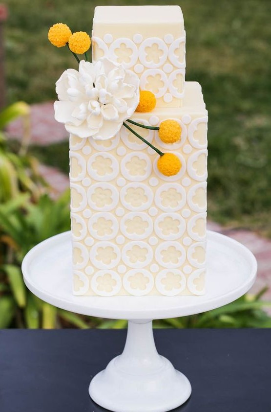 a pastel yellow and white patterned wedding cake decorated with a sugar flower and billy balls