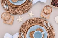 a pretty mermaid bridal shower table with a beige tablecloth and neutral napkins, woven placemats and wooden chargers, blue plates and mugs