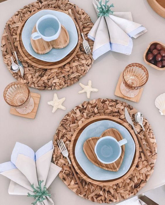 a pretty mermaid bridal shower table with a beige tablecloth and neutral napkins, woven placemats and wooden chargers, blue plates and mugs