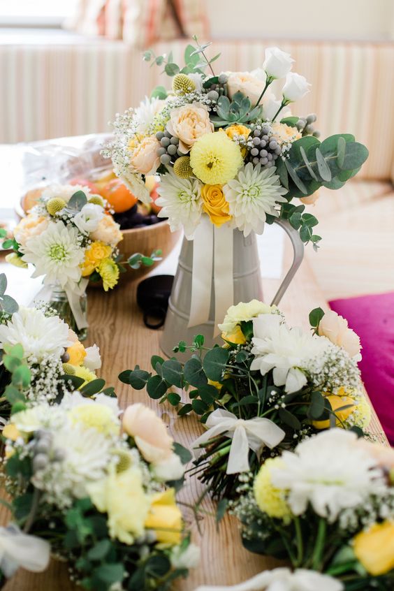 a pretty rustic summer wedding centerpiece of a metal jug, white, yellow blooms, greenery, billy balls and berries
