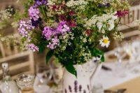 a pretty summer wedding centerpiece of a white jug with blooms painted and lots of wildflowers is a cool idea for a boho wedding