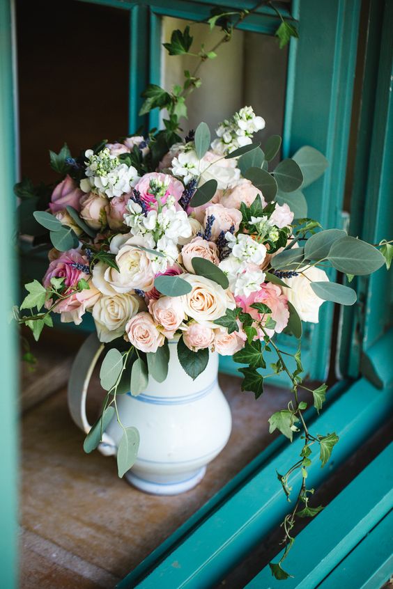 a romantic summer wedding centerpiece of a white and blue striped jug, blush and pink roses, greenery and lavender