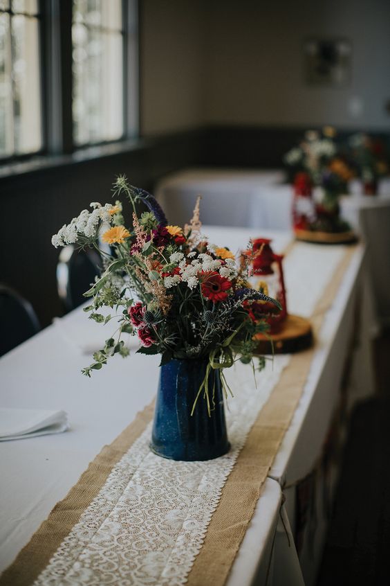 a rustic boho wedding centerpiece of a metal jug with bright wildflowers and greenery is a cool centerpiece idea