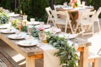 a rustic dining set with a fabric and a greenery runner and pink glasses for a cowgirl bridal shower