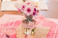 a simple bridal shower centerpiece of a jar with pink ribbons and pink blooms and a pink candle plus pink linens