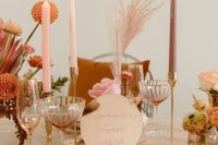a warm-colored retro wedding tablescape with pink plates, pink and mauve candles, bright orange blooms and metallic touches