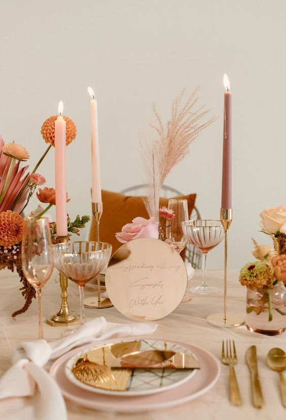 a warm-colored retro wedding tablescape with pink plates, pink and mauve candles, bright orange blooms and metallic touches