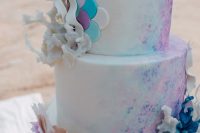a white wedding cake with pink, purple and turquoise splashes, scallops, corals and ruffles is an amazing idea for your bridal shower
