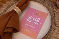 a woven palcemat, a neutral plate, a colorful card and a rust-colored napkin with a woven napkin ring is a catchy idea for a retro bridal shower