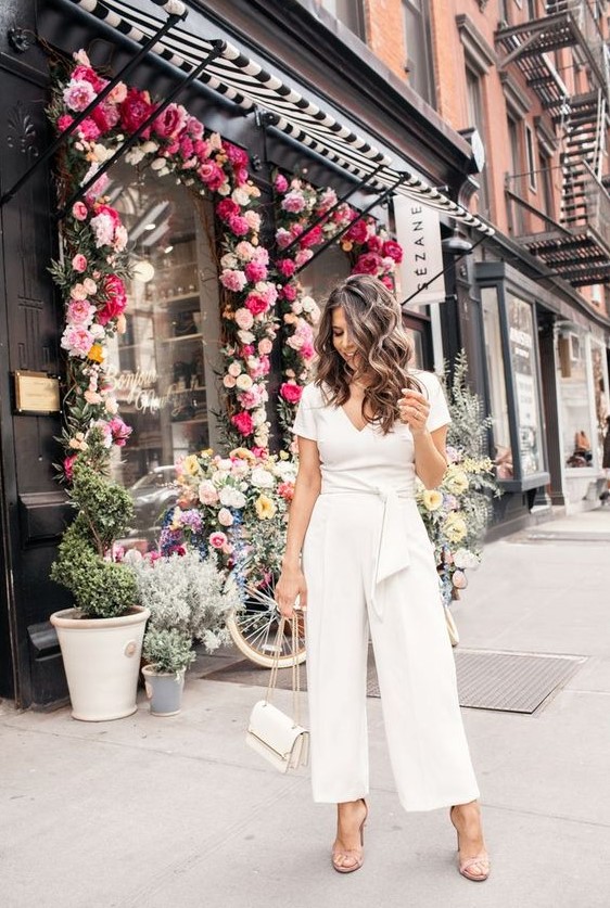 A casual white jumpsuit with a V neckline, short sleeves, wideleg pants, nude shoes and a white bag