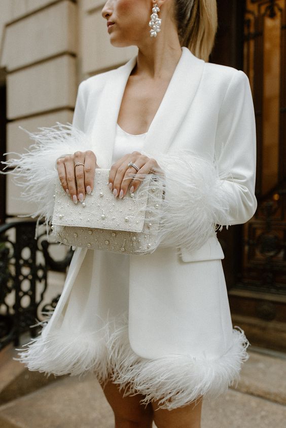 a white mini dress with feathers, a white blazer with feathers on the sleeves, a pearl bag and earrings