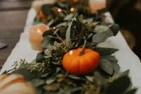 a beautiful fall rustic wedding table runner of eucalyptus, pumpkins, LED lights and candles is a lovely solution