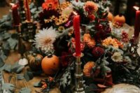 a beautiful rustic fall wedding centerpiece of white dahlias, orange and burgundy mums, greenery and tall and thin candles is adorable