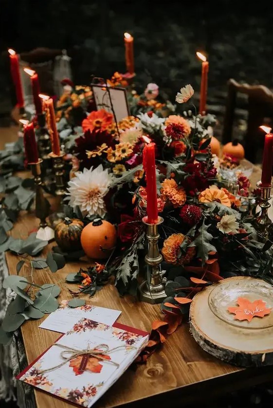 a beautiful rustic fall wedding centerpiece of white dahlias, orange and burgundy mums, greenery and tall and thin candles is adorable
