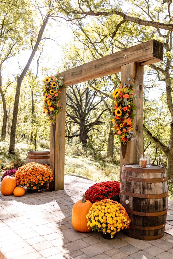 a bold rustic wedding arch of wood, with bright blooms and greenery, bold potted flowers and pumpkins