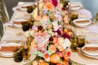 a bright fall wedding tablescape with a champagne runner, fruit, pumpkins, bold blooms and candles and dark glasses just wows