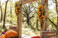 a bright rustic wedding arch with bold blooms and greenery, bold flowers and pumpkins and barrels is a cool idea