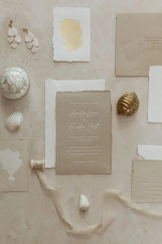 a chic coastal wedding invitation suite with a white envelope, beige cards, a godl coral print and a raw edge