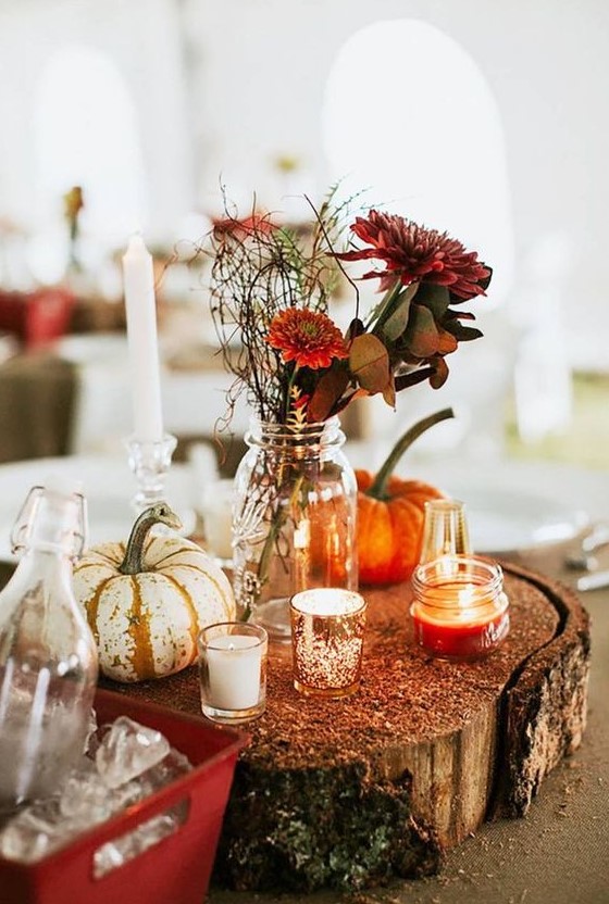 a chic fall wedding centerpiece of a wood slice, pumpkins, candles and burgundy flowers and greenery