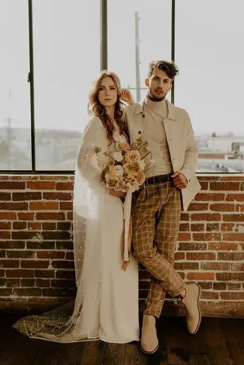 A creamy turtleneck, a creamy jacket, rust colored windowpane pants, tan Chelsea boots are a great look for a boho wedding
