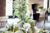 a creative fall wedding table with green and white pumpkins, greenery and leaves, neutral plates and greenery on the table