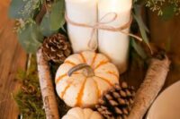 a cute DIY rustic wedding centerpiece of pumpkins, pinecones, branches, candles, baby’s breath and moss and greenery