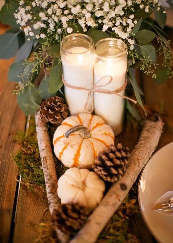 a cute DIY rustic wedding centerpiece of pumpkins, pinecones, branches, candles, baby's breath and moss and greenery