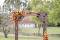 a fall backyard wedding ceremony space with a stained arch, bold blooms and greenery, pumpkins and potted blooms around it