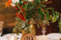 a fall centerpiece of a wood slice, acorns, pumpkins, candles, a wood slice table number and a bright floral arrangement
