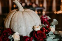 a fall wedding centerpiece of a large pumpkin, neutral and bold roses, berries and thistles, eucalyptus is amazing