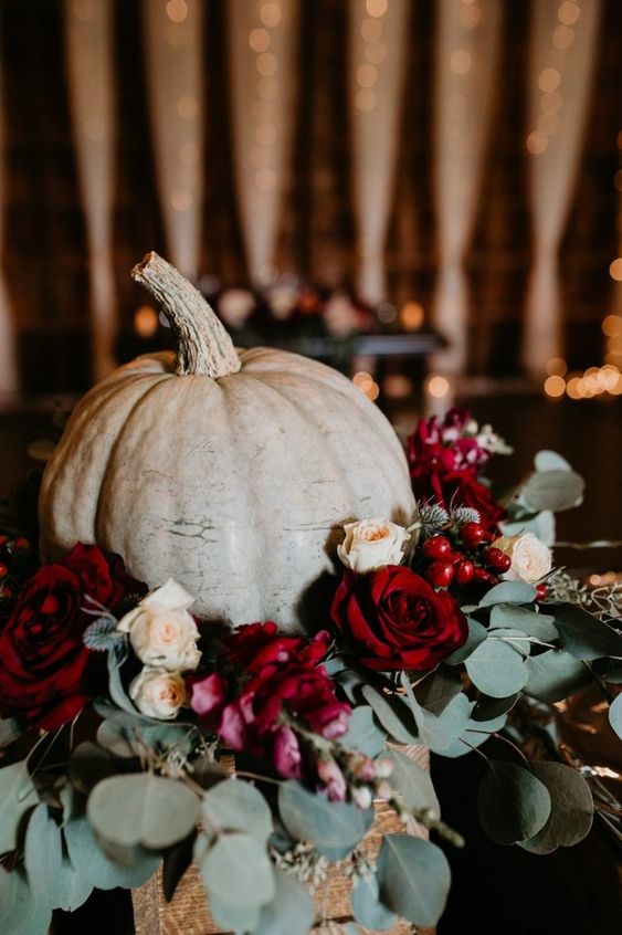 a fall wedding centerpiece of a large pumpkin, neutral and bold roses, berries and thistles, eucalyptus is amazing