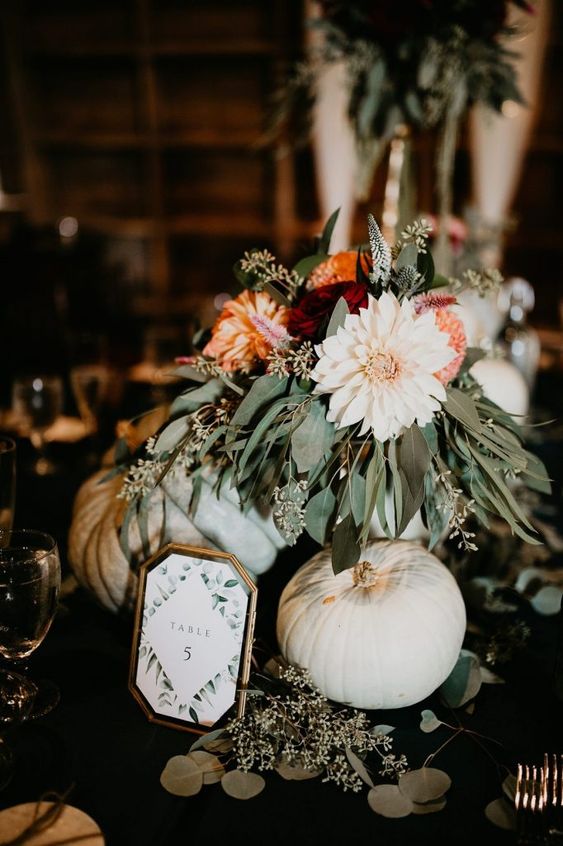 a fall wedding centerpiece of pumpkins, greenery, orange and blush blooms and a table number is a cool idea
