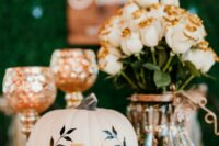 a fall wedding centerpiece of white roses with gold glitter in a vase, a white pumpkin with a letter and other decor