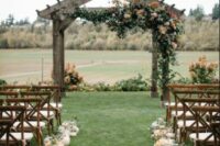 a fall wedding ceremony space with greenery and blooms, with pumpkins lining up the aisle and some greenery