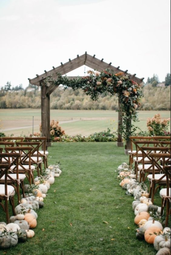 a fall wedding ceremony space with greenery and blooms, with pumpkins lining up the aisle and some greenery