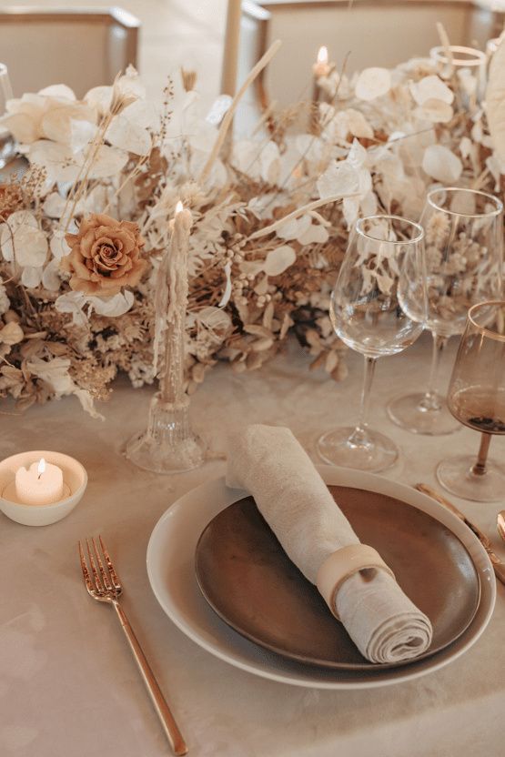 a fall wedding tablescape with a lush wedding centerpiece of fresh and dried blooms and grasses, candles, layered plates and neutral napkins